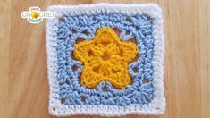 a crocheted square with a yellow and blue flower in the center on a wooden surface