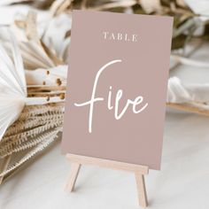 a table sign sitting on top of a wooden easel next to dried plants and paper fans