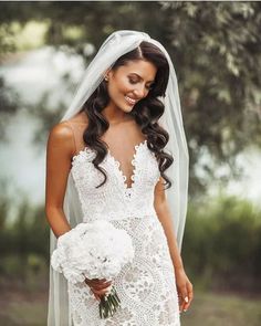 a woman in a wedding dress holding a bouquet and smiling at the camera while wearing a veil