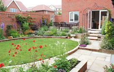 a garden with lots of flowers and plants in the grass next to a brick building