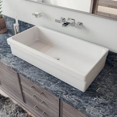 a white bathroom sink sitting on top of a counter next to a mirror and potted plant