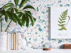 a green plant sitting on top of a white shelf next to a painting and books