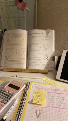 an open book sitting on top of a desk next to a calculator and cell phone