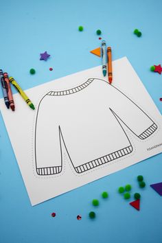 a paper cut out of a sweater with crayons next to it