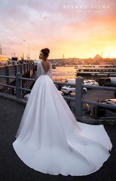 a woman in a white wedding dress standing on a pier at sunset with her back to the camera