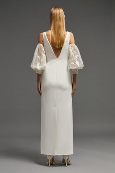 the back of a woman's white dress with sheer sleeves and an open shoulder