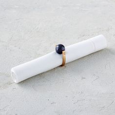 a white napkin with a black bead on it sitting in the sand next to a roll of paper