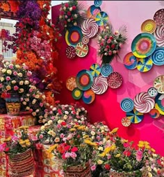 many colorful flowers are on display in front of a wall with paper plates and vases