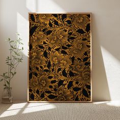 a gold and black wall hanging next to a vase with a plant in it on top of a carpeted floor