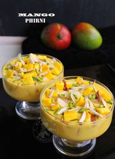 mango and pistachio dessert in small glasses on a black table with fruit behind them