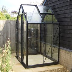 a small black glass greenhouse in front of a house