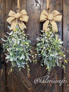 two wreaths with bows are hanging on a wooden door, decorated with greenery