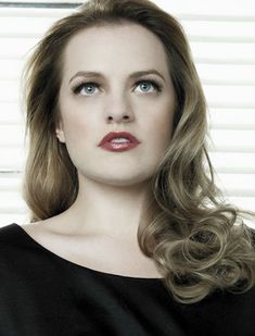 a woman with blonde hair and blue eyes posing for a photo in front of blinds