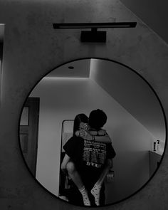 two people hugging each other in front of a round mirror with the reflection of them