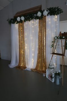 a white and gold wedding backdrop with flowers, greenery and lights on the wall