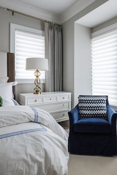 a bed room with a neatly made bed and a chair in front of the window