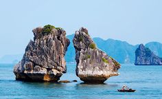 two large rocks sticking out of the ocean with people in small boats on them and mountains in the background