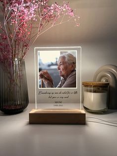 a vase with pink flowers in it next to a candle and a photo on a wooden stand