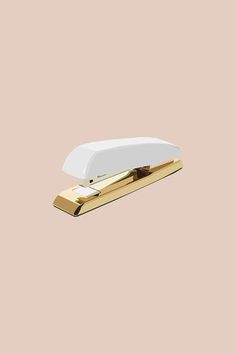 a white and gold stapler on a pink background