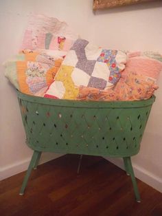 a green basket filled with lots of different colored quilts on top of a wooden floor