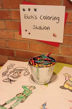 a bucket filled with crayons sitting on top of a table next to a sign