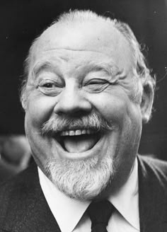 black and white photograph of an old man with a smile on his face, wearing a suit and tie