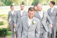 a group of men standing next to each other wearing grey suits and white flowers in their hair