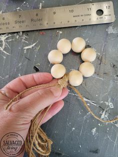 a hand holding some white beads on top of a piece of string next to a ruler