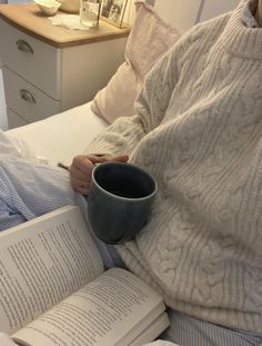 a person laying in bed with an open book and coffee cup on top of them