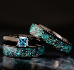 two wedding bands with blue and green glitters on them, one has a princess cut diamond in the center