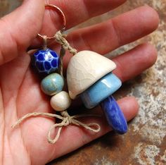 a hand is holding three small ceramic mushrooms and one has a blue glass bead on it