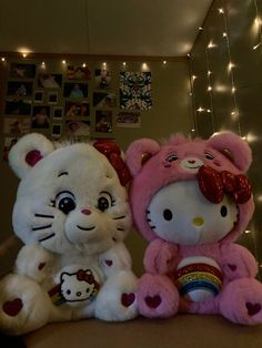 two hello kitty stuffed animals sitting next to each other on a table with christmas lights in the background