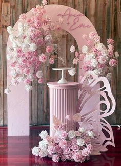 a pink vase with flowers and a butterfly decoration on the top is sitting in front of a wooden wall