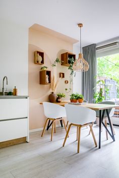 a dining room table with white chairs and plants on the shelves above it, in front of a window