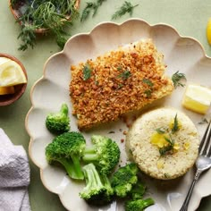 a white plate topped with food next to broccoli and lemon wedged potatoes