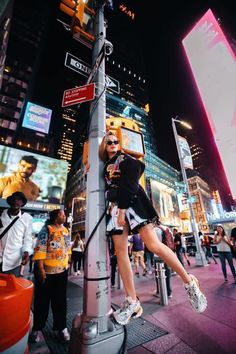 a woman leaning up against a pole in the middle of a busy city at night