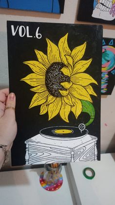 a person holding up a drawing of a sunflower on top of a record player