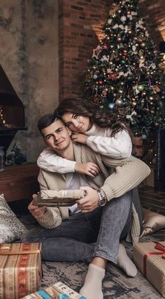 a man and woman sitting in front of a christmas tree with presents on the floor