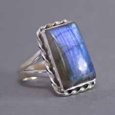 SKU: SS-025Material: 925 stamped sterling silverGemstone(s): Labradorite (N)Gemstone Dimensions: 14 X 21 X 4 mmRing Size: US 9Weight: 9.6 gramsThis captivating Labradorite cabochon ring features a distinctive twist motif around the stone. The Labradorite glows with a strong deep blue fire. There is a large rainbow inclusion that when tilted at the right angle, reveals its glittery iridescent effect. It’s the stone’s secret shimmer! Rectangular Moonstone Ring For Anniversary, Sterling Silver Rings Untreated, Silver Rings With Rectangular Natural Stones, Silver Rings With Large Rectangular Stone, Silver Ring With Large Rectangular Stone, Sterling Silver Rings With Natural Stones In Rectangular Shape, Rectangular Moonstone Ring Gift, Sterling Silver Square Gemstone Ring, Silver Rectangular Moonstone Ring Gift