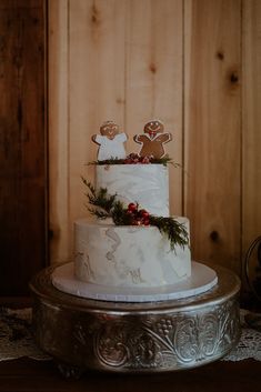 a three tiered white cake with gingerbread cookies on top and holly berries on the bottom