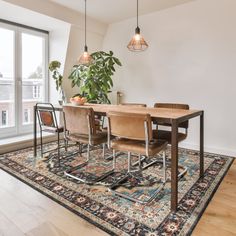 a dining room table and chairs in front of a large window with potted plants