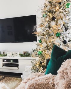 a white christmas tree with green and gold ornaments in front of a flat screen tv