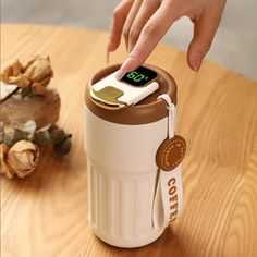 a person touching thermometer on top of a coffee cup that is sitting on a table