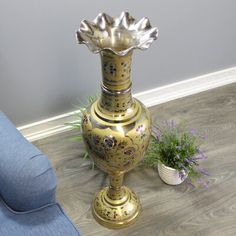 a gold vase sitting on top of a wooden floor next to a potted plant