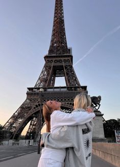 two women are standing in front of the eiffel tower, looking up at the sky