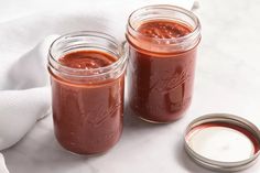 two jars filled with red sauce sitting on top of a white cloth next to a spoon