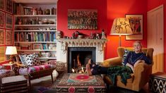 a woman sitting on a chair in front of a fire place and bookshelf