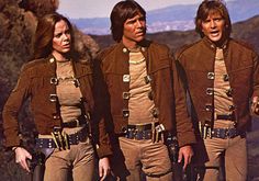 three men in brown uniforms standing next to each other with mountains in the back ground