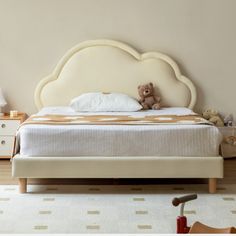 a bed with a teddy bear sitting on it's headboard in a bedroom