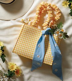 two yellow and white bags with blue ribbons on top of a bed next to flowers